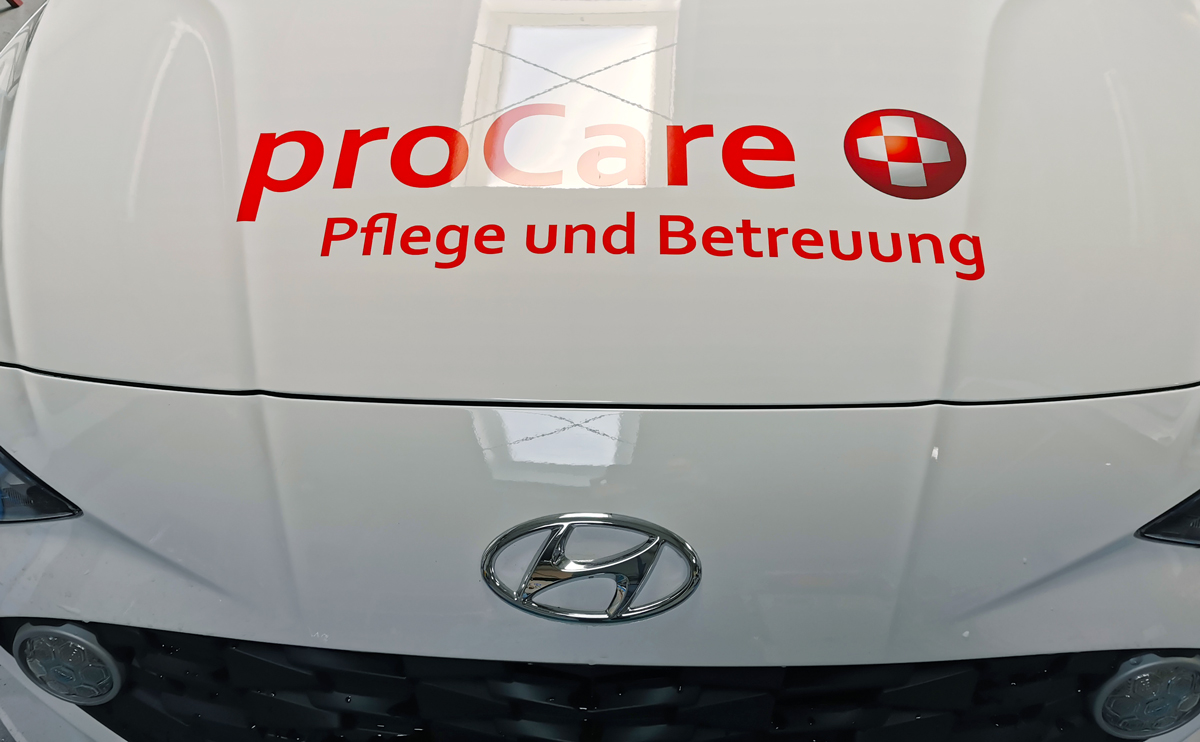 Autobeschriftung eines Hyundai i10 mit roter und grauer Folienschrift, sowie partiellen Digitaldruckaufklebern für das Pflege- und Beratungsunternehmen proCare in Grevenbroich-Elsen.